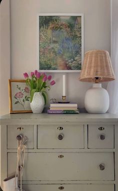 a white dresser with flowers and a lamp on top