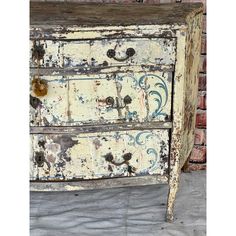 an old dresser with peeling paint on the top and bottom drawers is shown in front of a brick wall