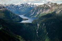 the mountains are covered with snow and green trees in the foreground is a lake surrounded by evergreens