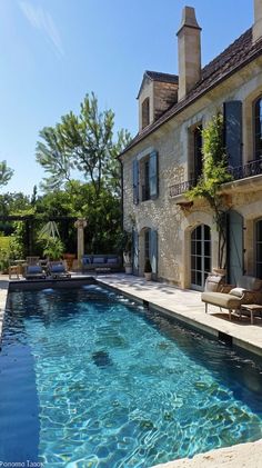 an outdoor swimming pool in front of a large stone house with french doors and windows