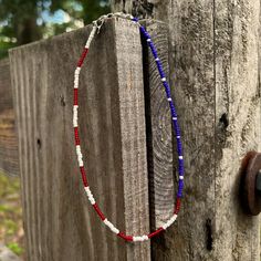 a red, white and blue beaded necklace hangs on a wooden fence