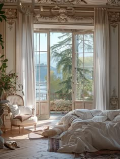 a bed sitting in a bedroom next to a large window covered in white sheets and pillows