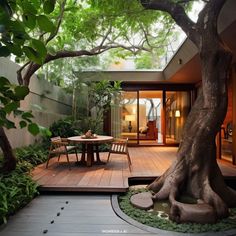 an outdoor dining area with wooden decking and large tree in the center, surrounded by greenery