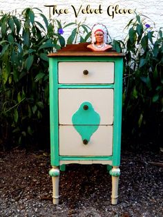 a green and white dresser sitting in front of some bushes