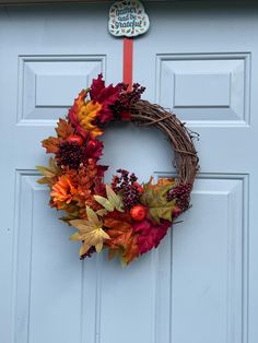 a wreath with autumn leaves and berries hanging on the front door to welcome you home