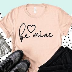 a t - shirt with the word be mine written in black on it next to some shoes