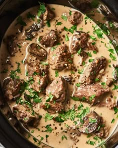 a crock pot filled with meat and mushrooms in gravy, garnished with parsley