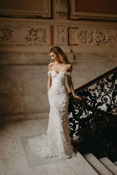 a woman in a white wedding dress standing on stairs with her hand on the railing