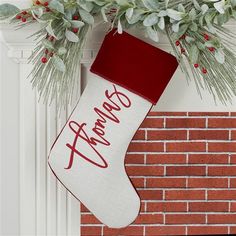 a christmas stocking hanging from a fireplace with greenery and berries on it's side