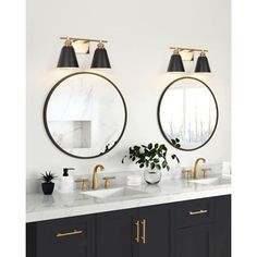 two round mirrors on the wall above double sinks in a bathroom with black cabinets and gold fixtures