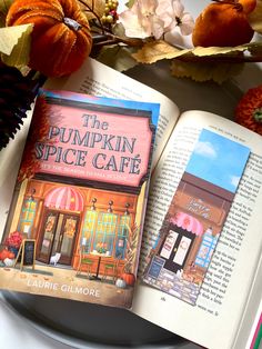 an open book sitting on top of a white plate next to flowers and pumpkins