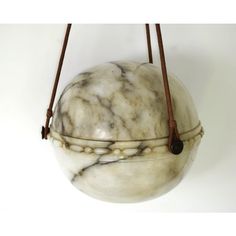 a white marble ball hanging from a brown leather cord on a white wall with a black bead around it