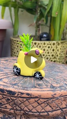 a yellow toy car sitting on top of a wooden table next to potted plants