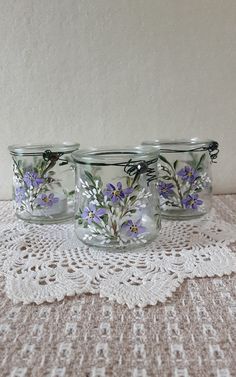 three glass jars with flowers painted on them sitting on a doily next to a wall