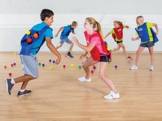 a group of young people playing with balls in an indoor gym area on a hard wood floor