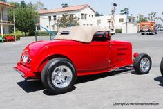 an old red convertible car parked in a parking lot next to another classic model car