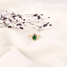 a green ring sitting on top of a white cloth next to some dried flowers and branches