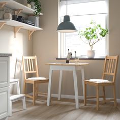 two wooden chairs sit at a small table in front of a window with a potted plant on it