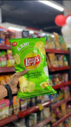 a hand holding a bag of lay's potato chips in a grocery store aisle