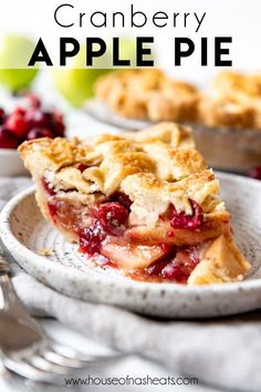 a slice of pie on a plate with cranberries and apples in the background