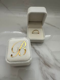 an open ring box sitting on top of a marble counter next to a gold monogrammed ring