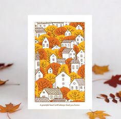 a card with an image of houses and trees in the fall colors, surrounded by leaves