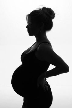 a pregnant woman standing in silhouette with her hands on her hips