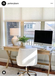 a desk with a computer on top of it in front of a window next to a potted plant