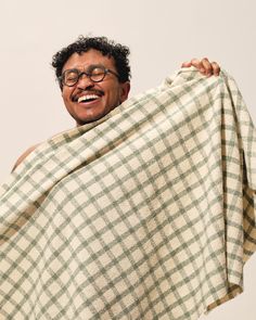 a man with glasses holding up a plaid blanket over his head and smiling at the camera