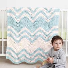 a baby sitting on the floor next to a crocheted blanket