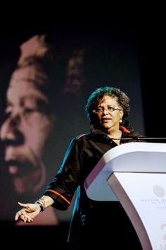 a woman standing at a podium in front of a screen with a man's face on it