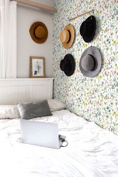 a laptop computer sitting on top of a bed next to hats hanging on the wall