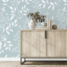 a white vase with flowers on top of a wooden cabinet in front of a blue wall