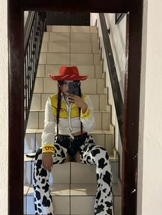 a woman in cow print pants and cowboy hat taking a selfie with her cell phone