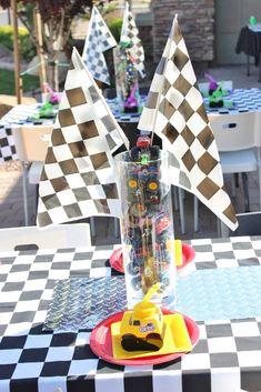 the table is decorated with checkered black and white tables cloths, yellow plastic toy cars in a glass vase