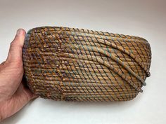 a hand is holding a woven basket with blue and brown lines on it's sides