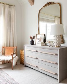 a white dresser sitting next to a window in a room with a mirror on top of it