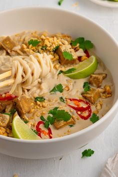 a white bowl filled with noodles, meat and garnished with cilantro