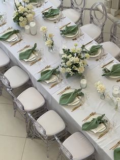 a long table with white chairs and green napkins is set for a formal dinner