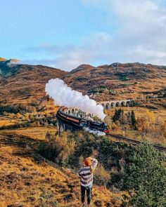 a man standing on the side of a hill looking at a train coming down it's track