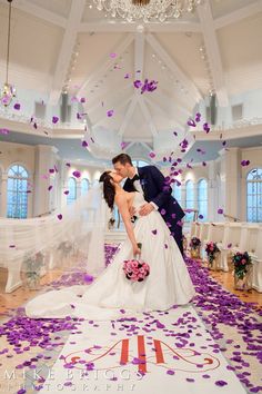 a bride and groom kissing in front of purple confetti on the dance floor