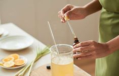 a woman is holding a glass with some liquid in it and an orange slice on the table