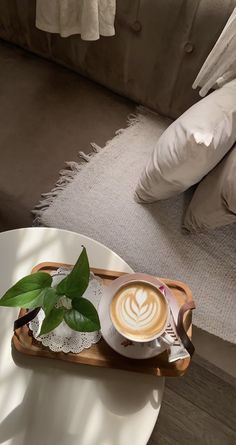 a cup of coffee sitting on top of a wooden tray next to a white couch