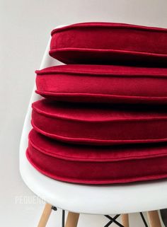 four red pillows stacked on top of each other in front of a white chair with wooden legs