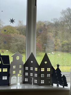 three paper houses sitting on top of a window sill next to a green field