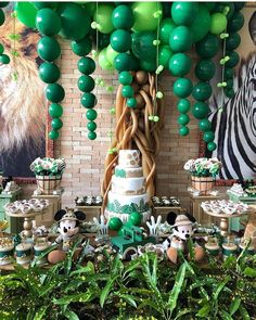 a jungle themed birthday party with green balloons, cake and cupcakes on the table