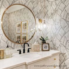 a bathroom with marble wallpaper and gold accents on the vanity, along with a round mirror