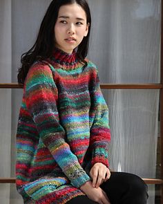 a woman sitting on a window sill wearing a multicolored sweater and black pants