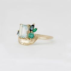 The 'Mint Blush' ring from the Impasto Collection is a symphony of color and craftsmanship in 14K yellow gold, size 6.25. It features a central 0.95ct emerald-cut aquamarine, exuding serene elegance. The ring is adorned with a spectrum of precious stones: twin G/H VS2 diamonds totaling 0.01 carats, a 0.12ct baguette aquamarine, a 0.05ct marquise blue tourmaline, along with a 0.12ct marquise and a 0.12ct round emerald, each contributing to the ring's lush palette. Mint Tourmaline Ring, Emerald Cut Aquamarine Ring, Artisan Fashion, Vs2 Diamond, Blue Tourmaline, Aquamarine Ring, Aquamarine Rings, Tourmaline Ring, Jewel Box