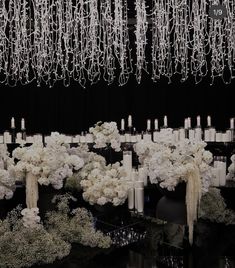 an arrangement of white flowers and candles in front of a black backdrop with chandelier